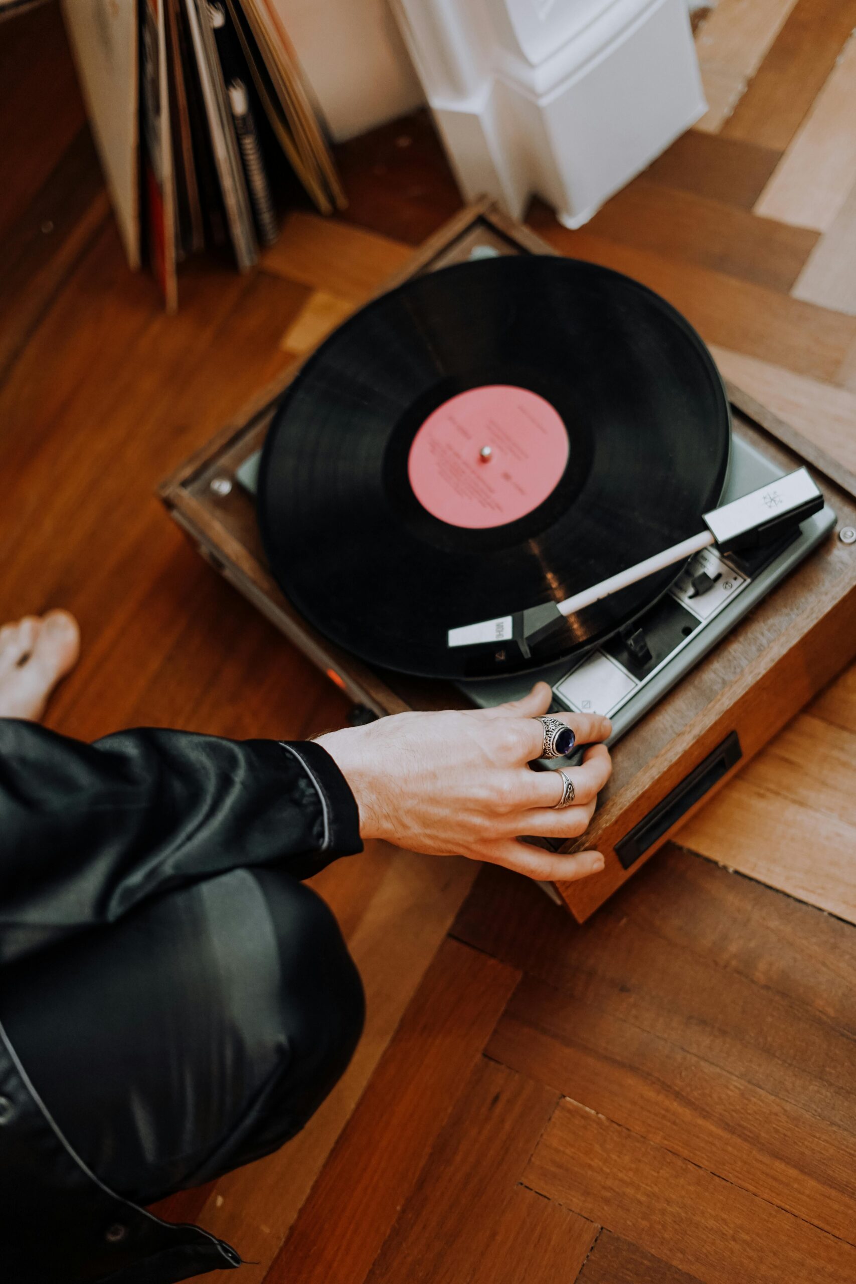 Person adjusting a vintage turntable playing a vinyl record on a wooden floor indoors.